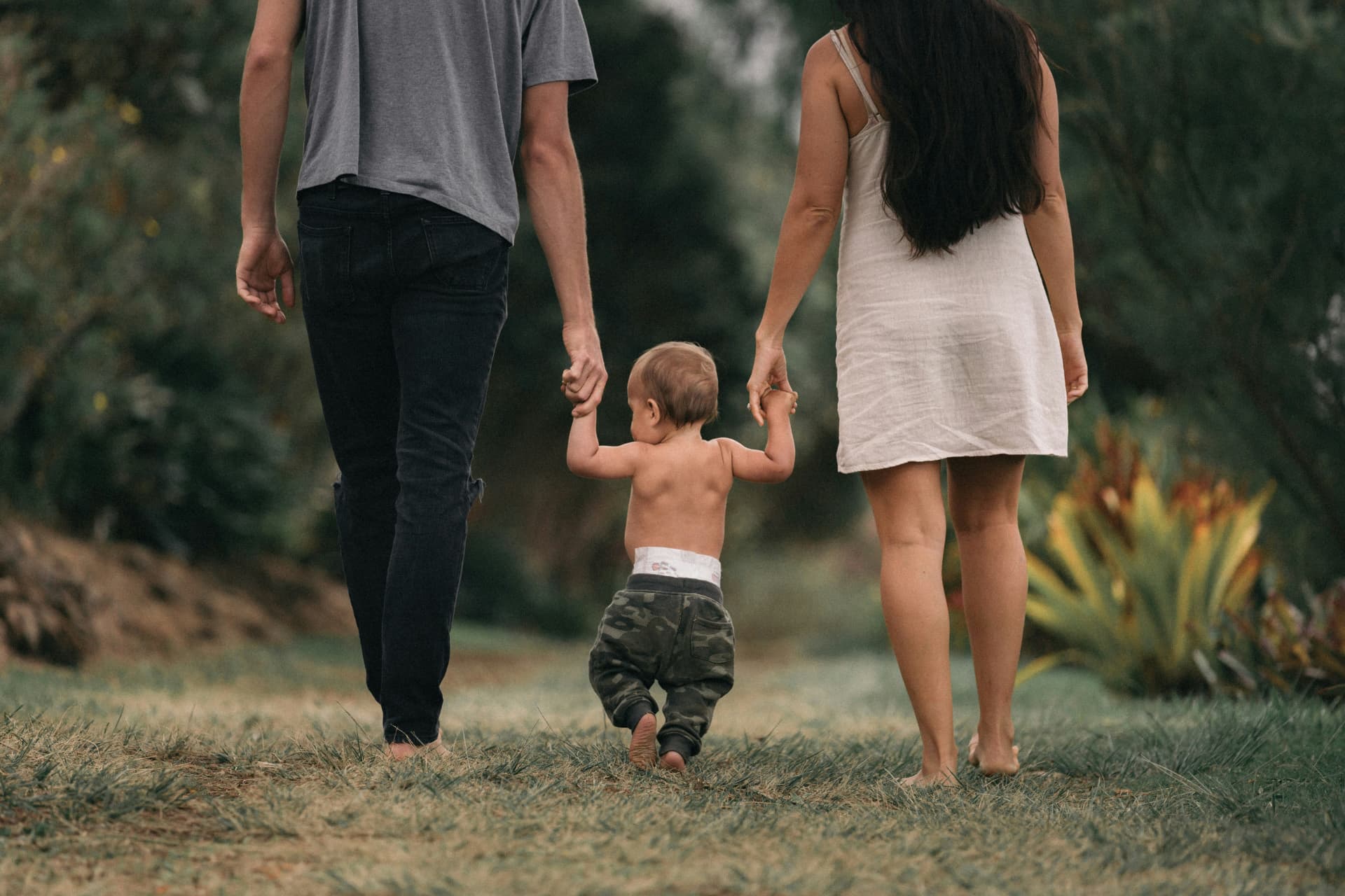 A couple walking barefoot with their young child through a garden path