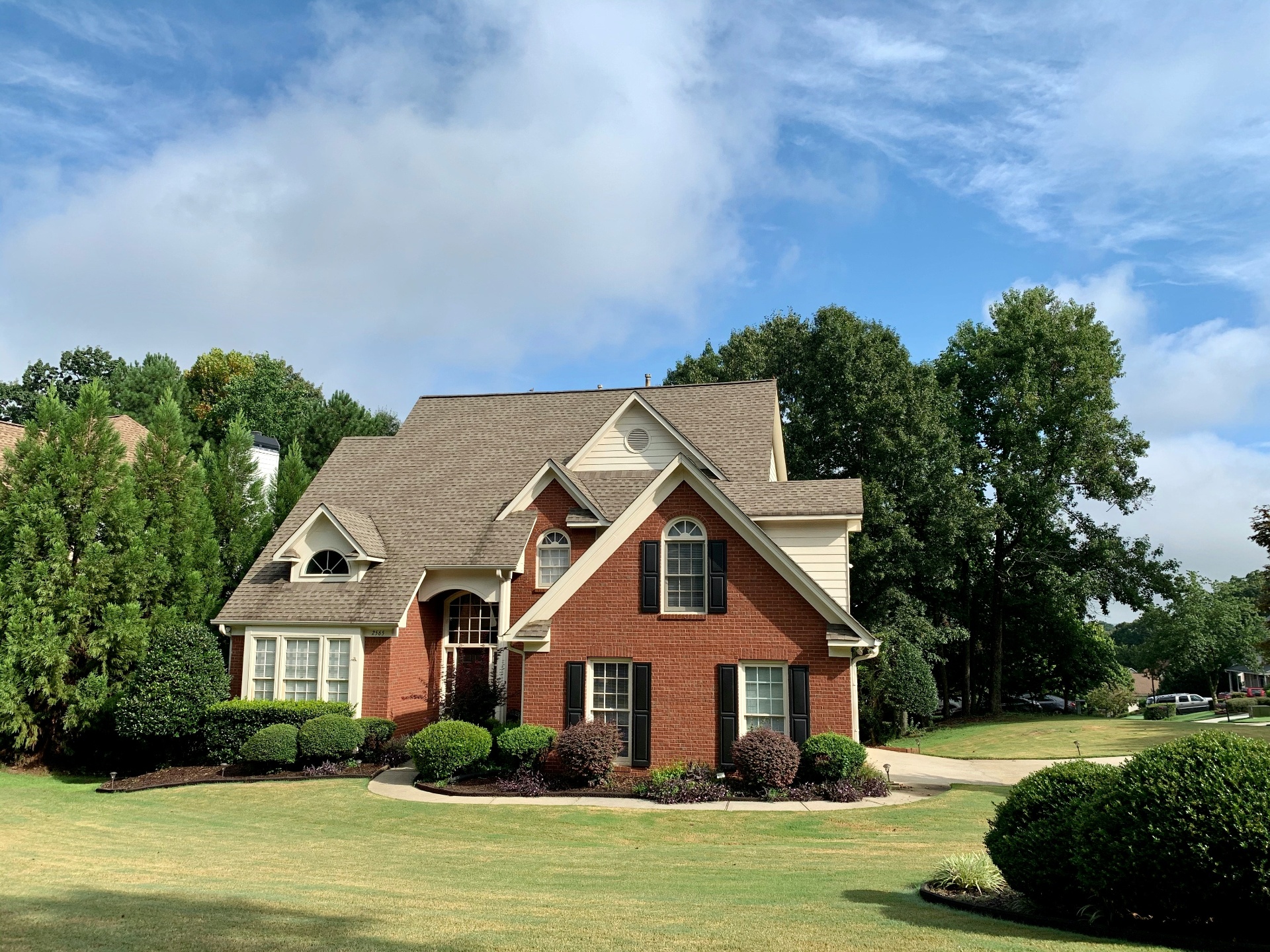 Brick house with manicured lawn and trees under a blue sky