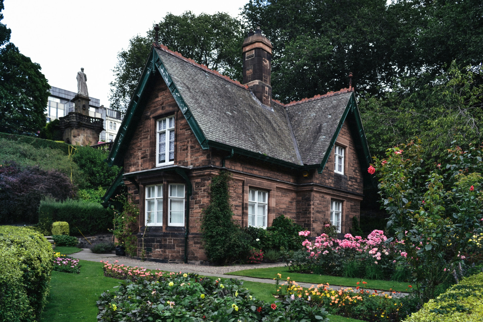 Brown and white stone cottage with a garden of roses in bloom